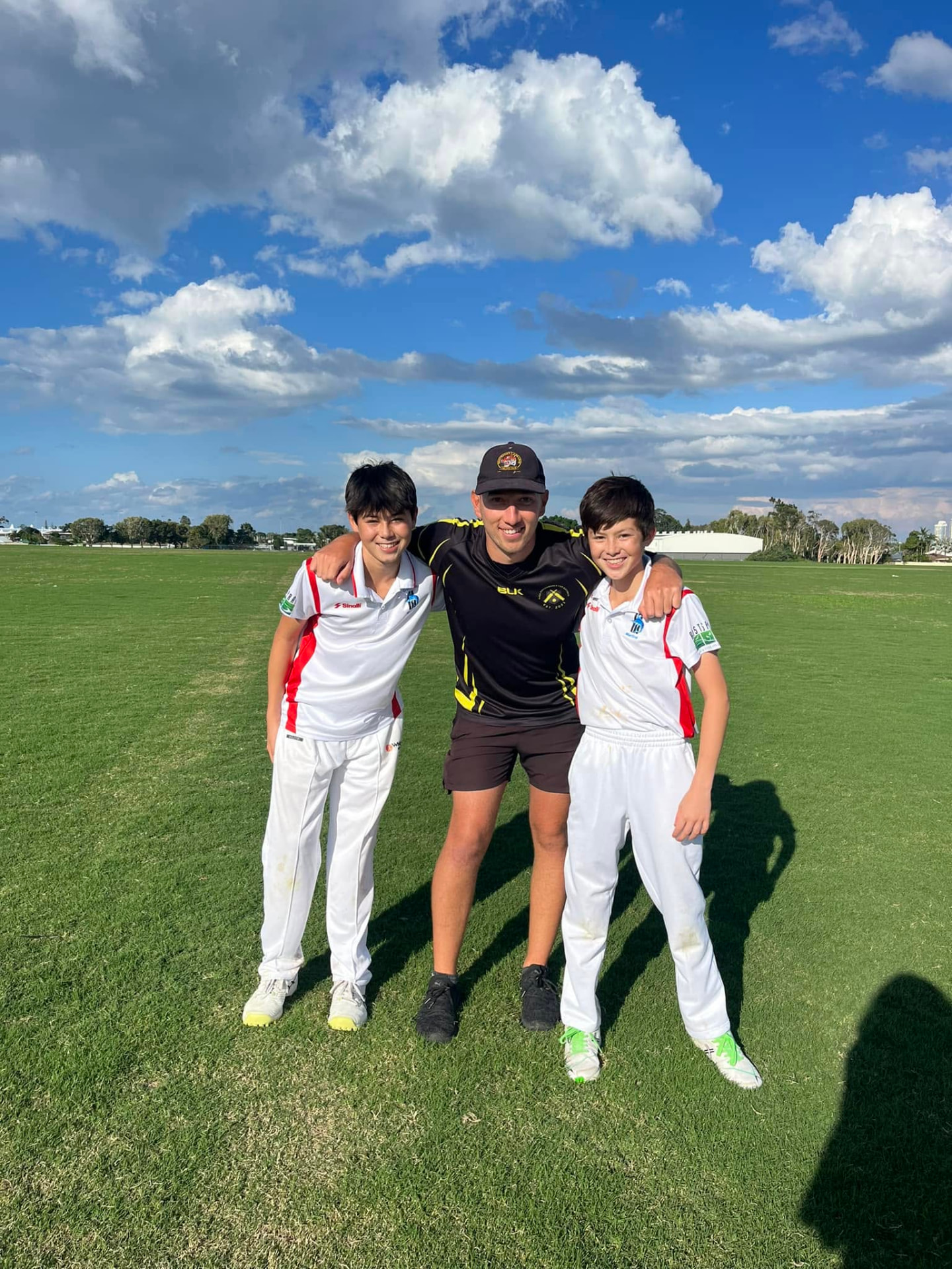 Jarrod with his arms around two young cricketers in whites
